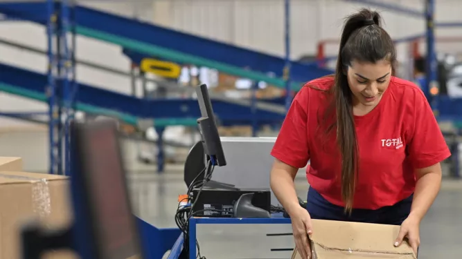Dicionário de logística: uma pessoa com camiseta da Total Express embalando produtos em uma caixa.