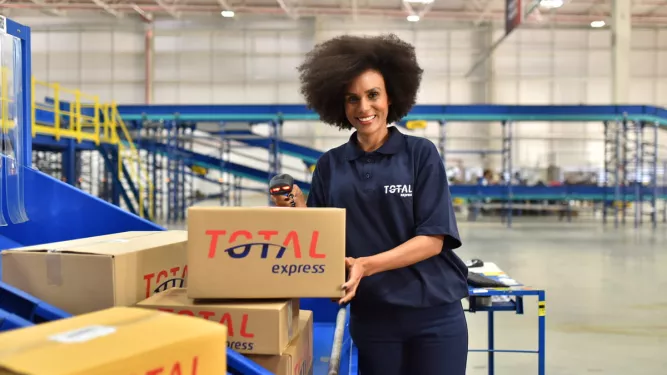 Uma mulher com roupa da Total Express mostrando as embalagens na logística.