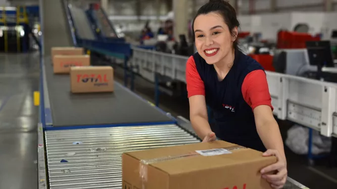 KPIs na logística: uma mulher embalando caixas com símbolo da Total Express.