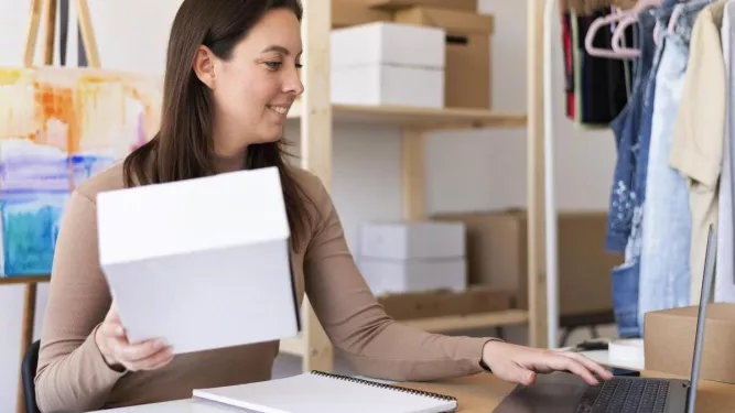 Mulher segurando uma caixa e usando um laptop, representando o conceito de "o que é frete" no e-commerce.
