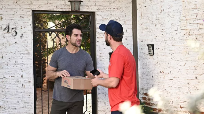 Cliente e entregador conversam na porta de casa durante a devolução de mercadoria, conferindo detalhes da encomenda.