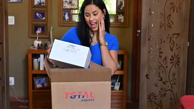 Mulher surpresa ao abrir embalagem de presente no Dia das Mães, demonstrando alegria com a chegada da encomenda.