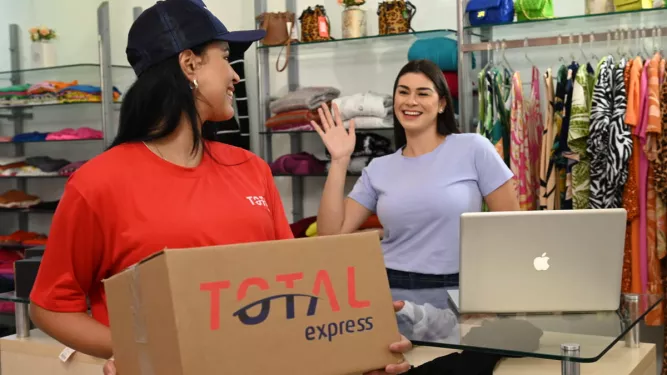 Funcionária de loja recebe pacote da transportadora, representando a etapa inicial da logística de entrega, conhecida como first mile.