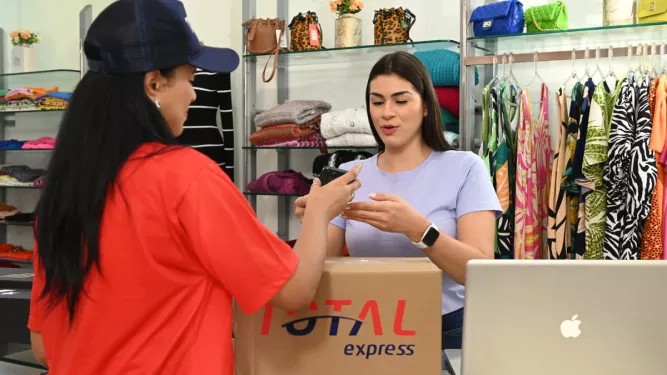 Funcionária de uma loja recebe um pacote da transportadora Total Express, ilustrando a rapidez do next day delivery para entregas eficientes no comércio.