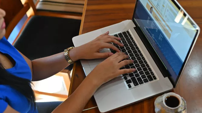 Imagem de uma pessoa digitando em um laptop, com café ao lado, acessando documentos de logística.