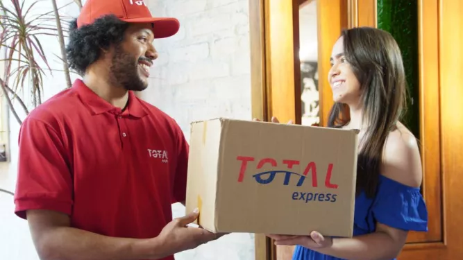 Entregador da Total Express sorri para a cliente enquanto faz a coleta de uma Total Reversa.