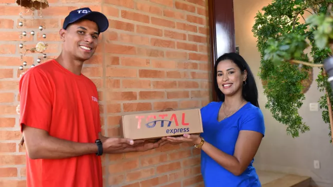 Total Solutions: Entregador da Total Express realizando a entrega de um pacote para o cliente, com ambos sorrindo na porta da residência.