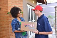 Mulher recebe caixa da Total Express com encomenda. O entregador faz uma logística sustentável