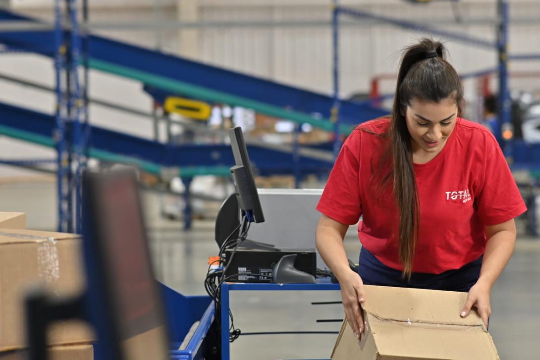 Dicionário de logística: uma pessoa com camiseta da Total Express embalando produtos em uma caixa.