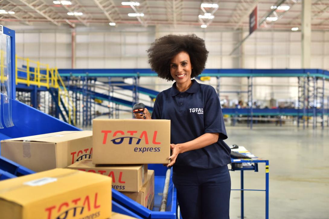 Uma mulher com roupa da Total Express mostrando as embalagens na logística.