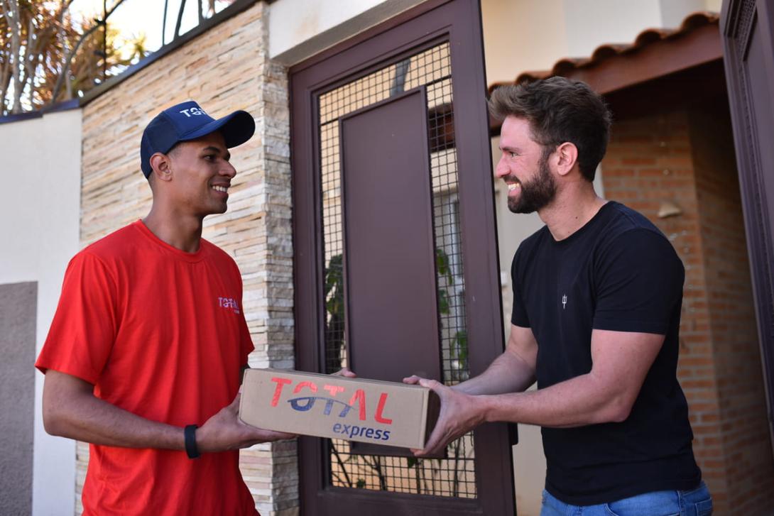 Logística para e-commerce: um entregador deixa a encomenda com o cliente na porta de sua casa.
