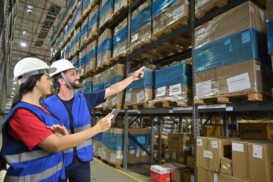 Na imagem, vemos duas pessoas com EPIs conversando sobre o processo de armazenagem.