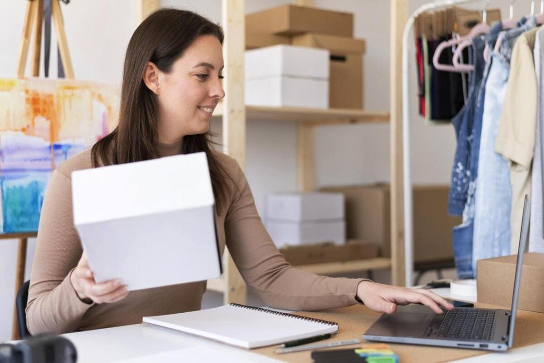 Mulher segurando uma caixa e usando um laptop, representando o conceito de "o que é frete" no e-commerce.