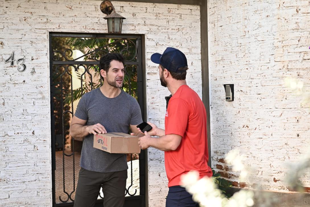 Cliente e entregador conversam na porta de casa durante a devolução de mercadoria, conferindo detalhes da encomenda.