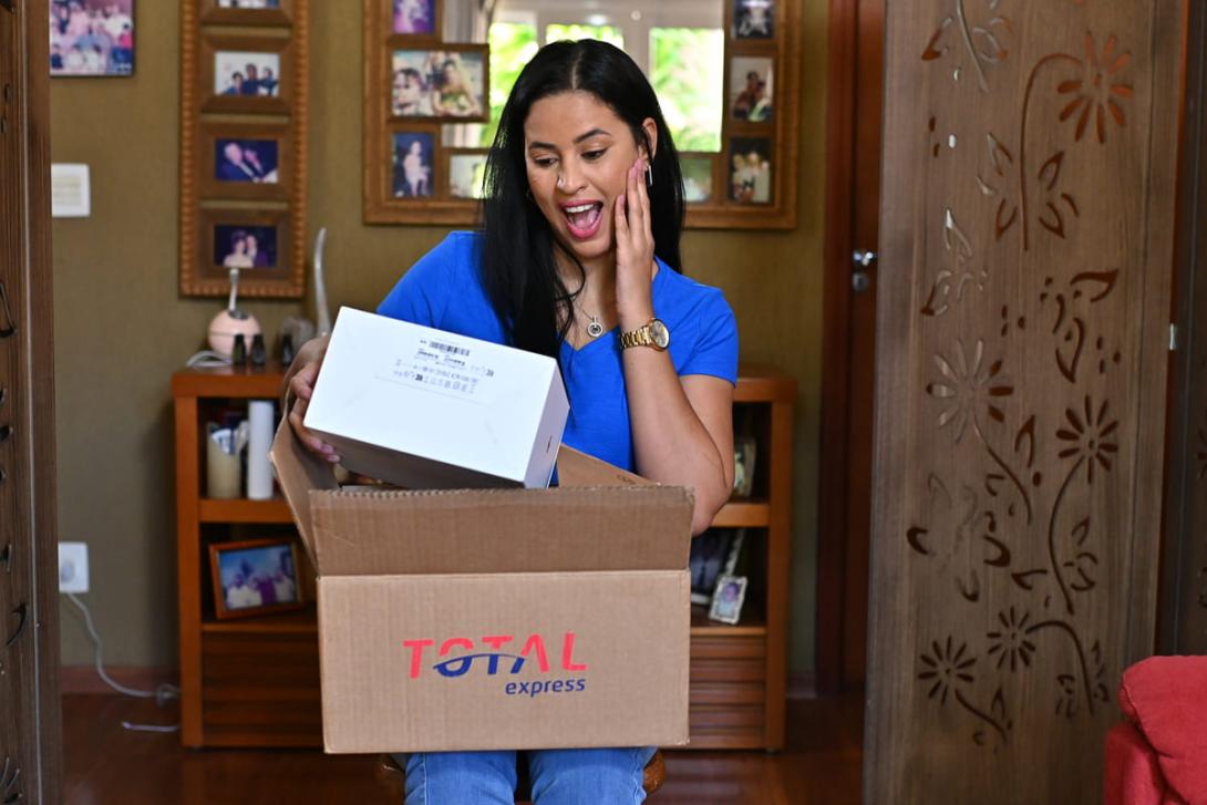 Mulher surpresa ao abrir embalagem de presente no Dia das Mães, demonstrando alegria com a chegada da encomenda.