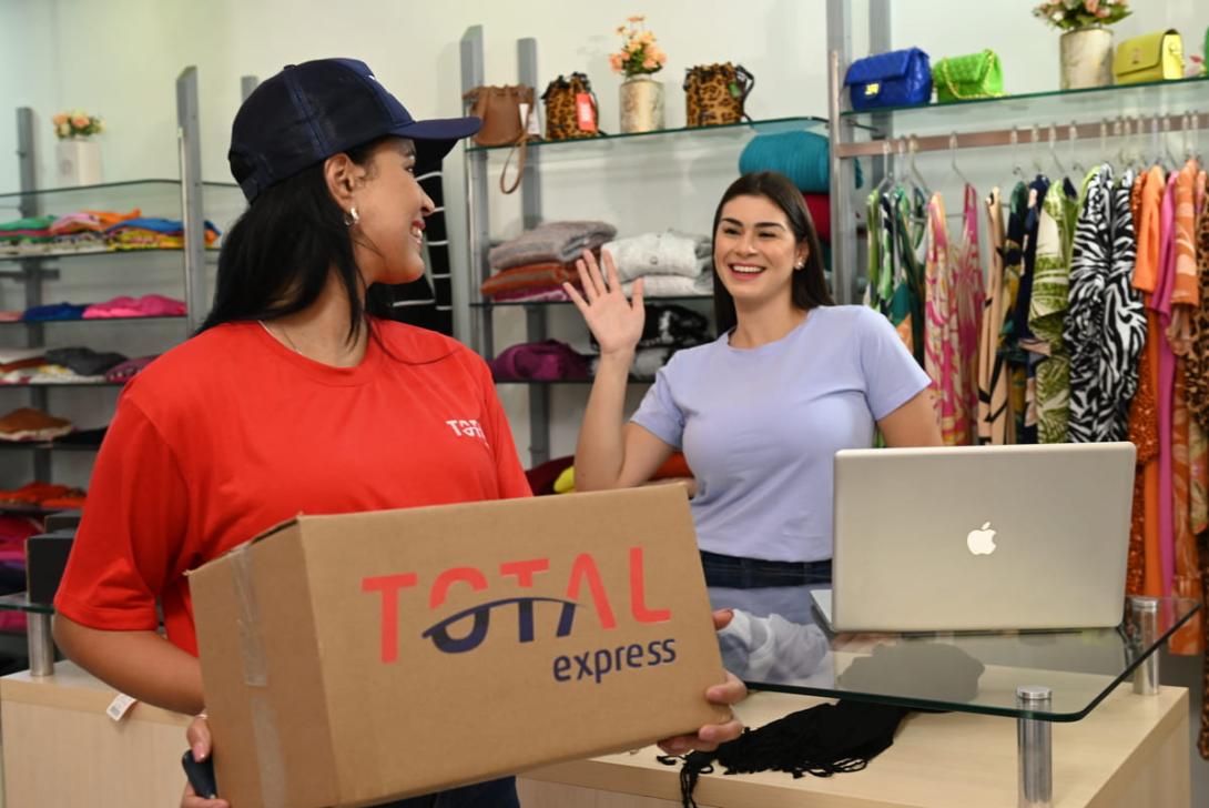 Funcionária de loja recebe pacote da transportadora, representando a etapa inicial da logística de entrega, conhecida como first mile.