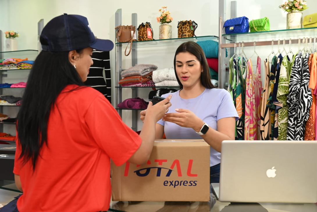 Funcionária de uma loja recebe um pacote da transportadora Total Express, ilustrando a rapidez do next day delivery para entregas eficientes no comércio.