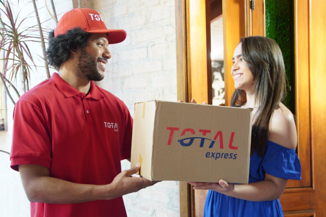 Entregador da Total Express sorri para a cliente enquanto faz a coleta de uma Total Reversa.