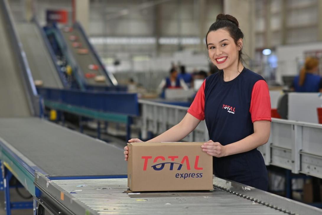 Funcionária de cross docking segurando caixa da Total Express em uma esteira 